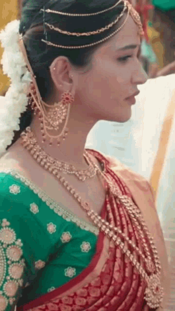 a close up of a woman wearing a red and green saree and jewelry .