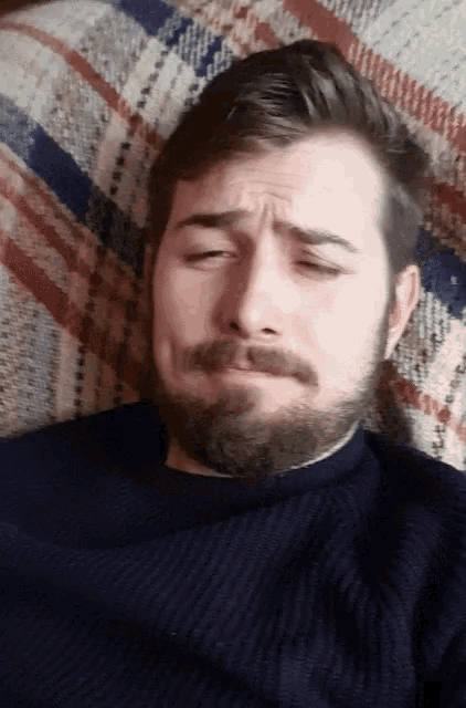 a man with a beard is laying on a plaid blanket