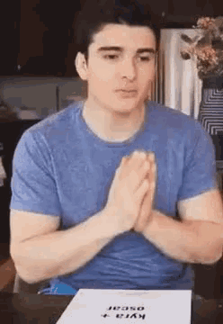 a man in a blue shirt is sitting at a table with his hands folded .