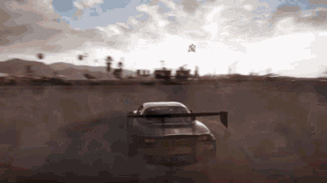 a car is driving down a dirt road with a wing on the back