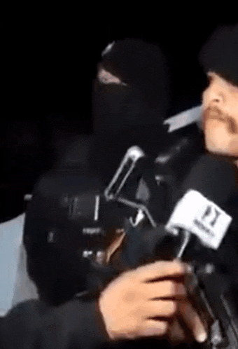 a man in a black mask is holding a microphone in front of a camera .