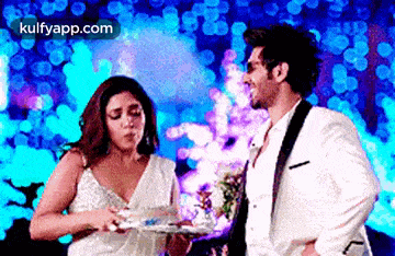 a man and a woman are standing next to each other . the woman is holding a plate of food .