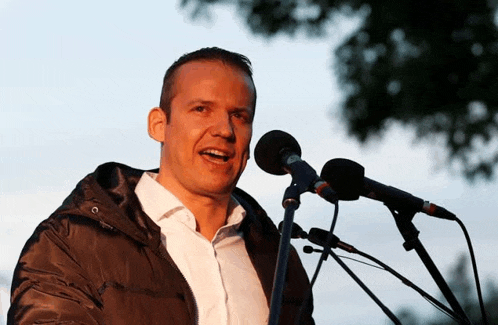 a man is speaking into a microphone with a hood on