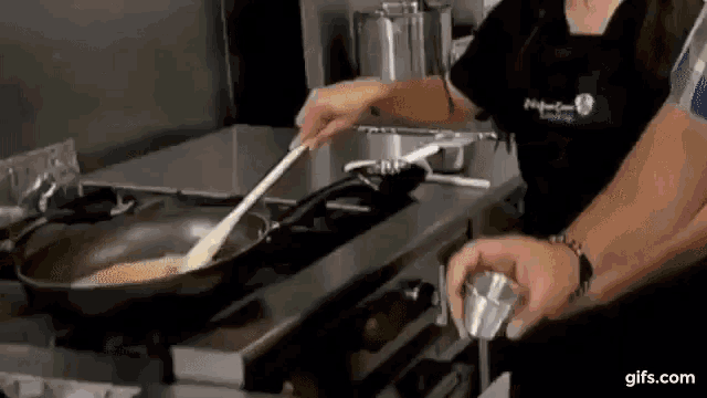 a woman is cooking food in a frying pan on a stove with a spoon .