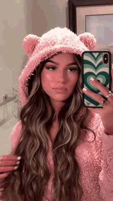 a woman taking a picture of herself in a mirror wearing a pink teddy bear hat