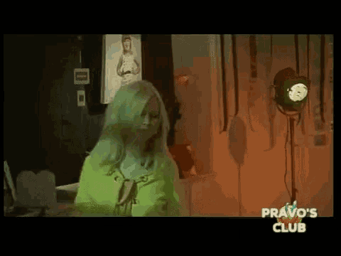 a woman with green hair is standing in a dark room with the words " pravo 's club " on the bottom right
