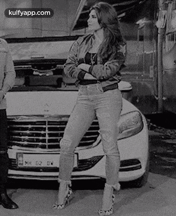 a black and white photo of a woman standing in front of a white car .