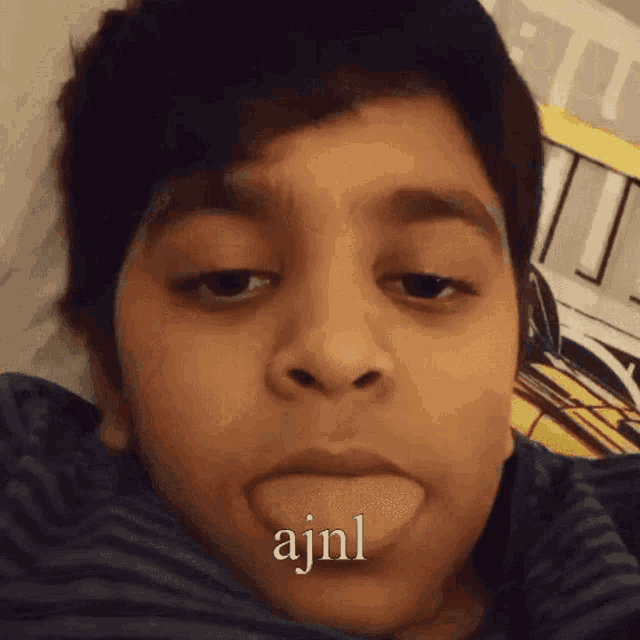 a young boy is sticking his tongue out and the word ajnl is on his face