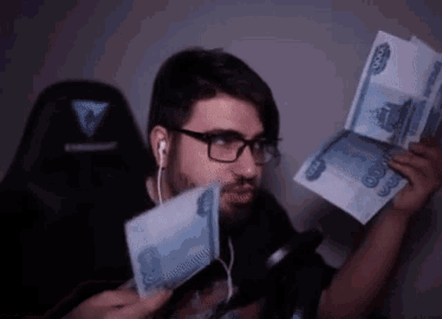 a man wearing glasses and headphones is holding a bunch of money in his hands .