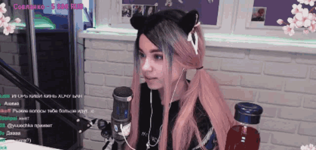 a girl with pink hair is sitting in front of a microphone with flowers in the background and a sign that says 5 000 rub