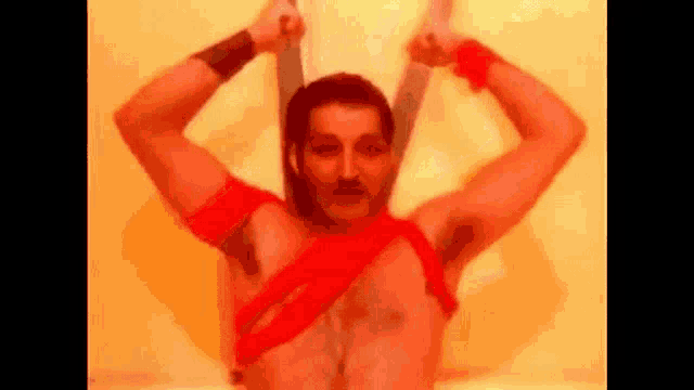 a shirtless man is holding two swords over his head while wearing a red harness .