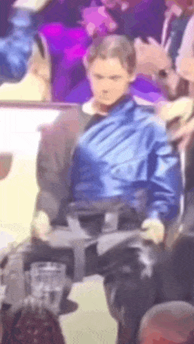 a man in a blue jacket and leather pants is sitting in a crowd of people .