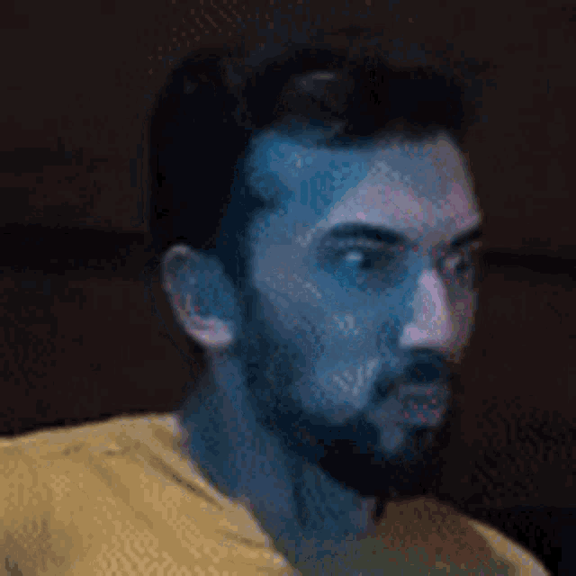 a man with a beard and sunglasses is wearing a yellow shirt and looking at the camera .