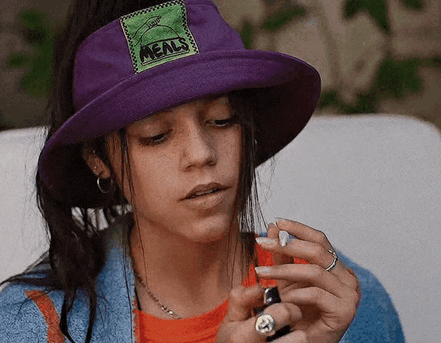 a woman in a purple hat is lighting a cigarette