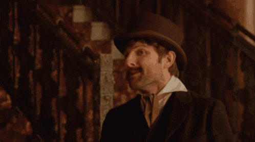 a man with a hat and a mustache holds a cigarette