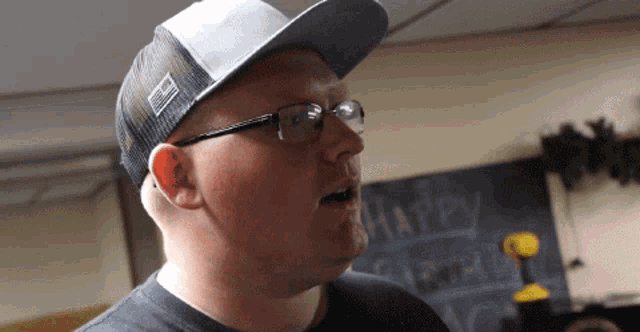 a man wearing a hat and glasses is standing in front of a chalkboard that says happy birthday