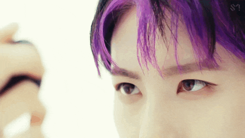 a close up of a man 's face with purple hair