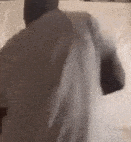 a man in a white shirt is standing in front of a white wall and holding a white shirt over his shoulder .