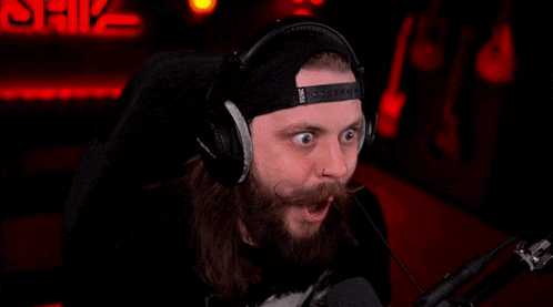 a man with a beard is wearing headphones and a hat and making a surprised face