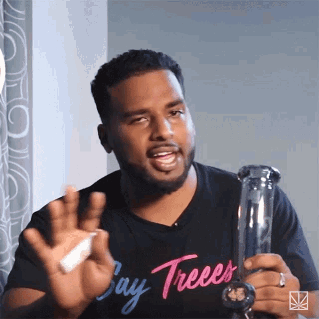 a man wearing a shirt that says bay trees holds a bong