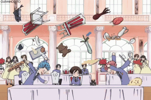 a group of people are sitting at a table with objects falling around them including a chair and a teddy bear