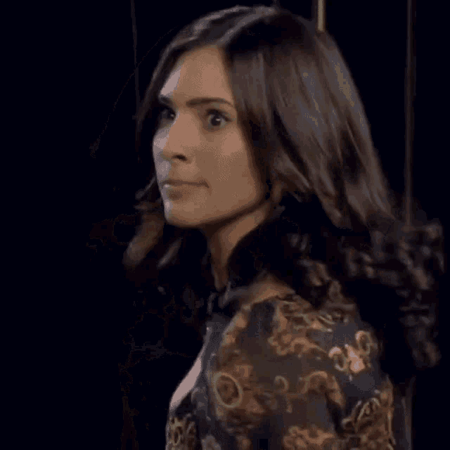 a woman in a floral dress is standing in front of a black wall and looking at the camera .