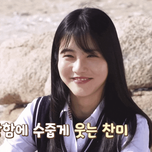 a girl with long black hair is smiling with korean writing behind her