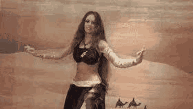 a woman with long hair is dancing belly dance in front of a painting of camels in the desert .