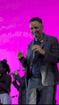 a man in a suit is singing into a microphone in front of a pink background .