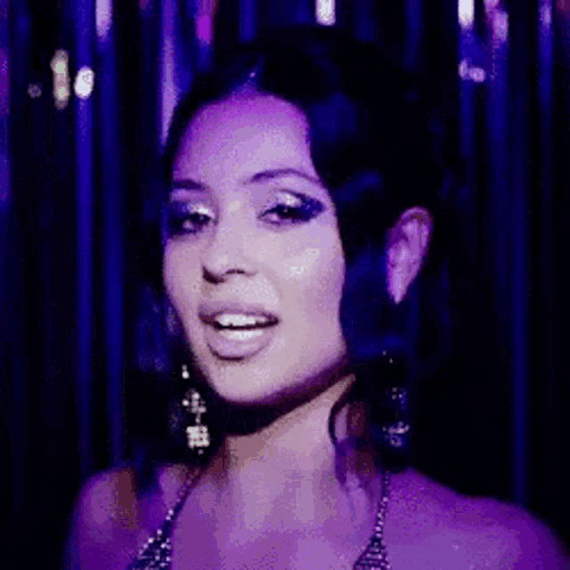 a woman in a purple dress is smiling in front of a purple background .