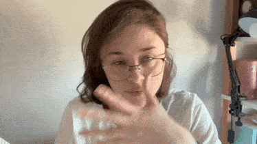 a woman wearing glasses and a white shirt is making a gesture