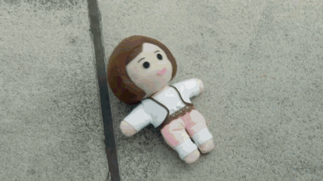 a stuffed doll is laying on the ground with a person 's hand behind it