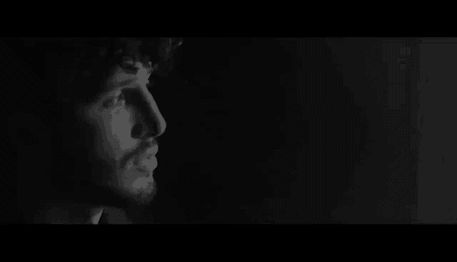 a black and white photo of a man with a beard looking out a window .