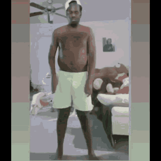 a shirtless man is standing in a living room wearing green shorts