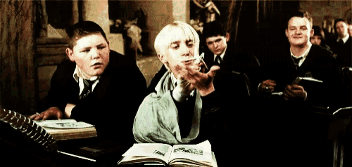 a group of boys are sitting in a classroom with a girl sitting in front of an open book