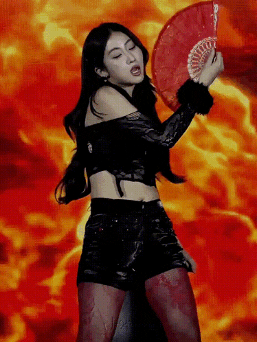 a woman in a black top and shorts is holding a red fan in front of flames