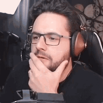 a man wearing glasses and headphones is sitting in a chair with his hand on his chin .