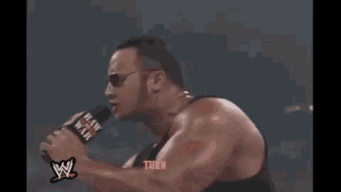 a man wearing sunglasses is standing in a boxing ring with a red rope .