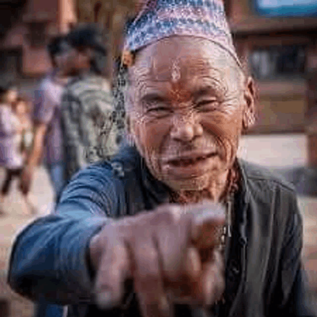 an elderly man wearing a hat is pointing his finger at the camera .