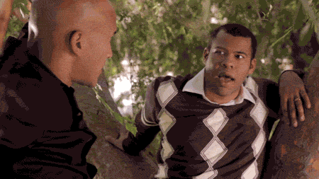 a man in a plaid sweater is talking to another man in a black shirt