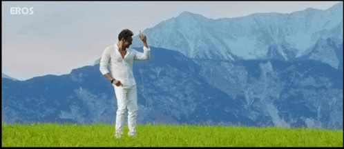 a man in a white shirt is dancing in a field with mountains in the background and eros written on the bottom
