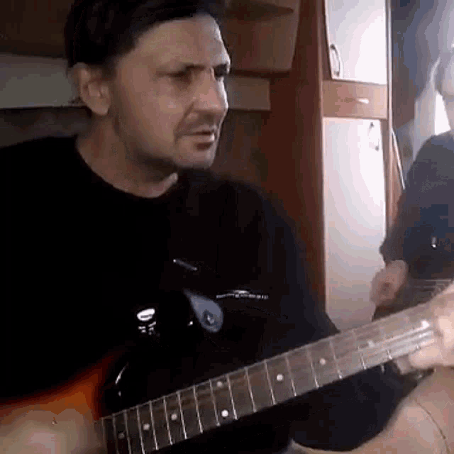 a man in a black shirt is playing an electric guitar in a room .