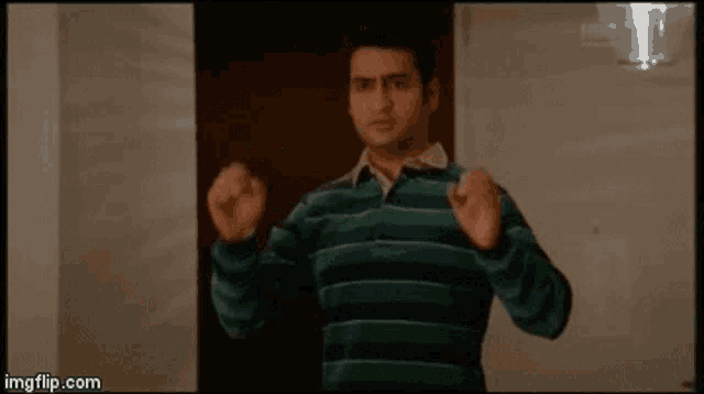 a man in a green and blue striped shirt is standing in front of a door with his fist in the air .