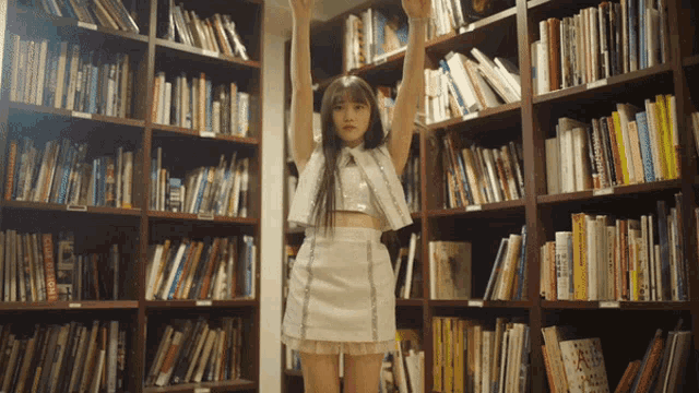 a woman in a white dress is standing in a library surrounded by bookshelves