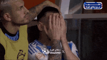 a soccer player covering his face with his hands while another player watches