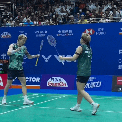 a man and a woman are playing badminton on a court with advertisements for ganten and hsbc