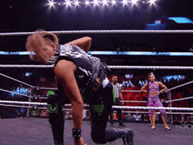 a woman is kneeling down in a wrestling ring while a referee watches