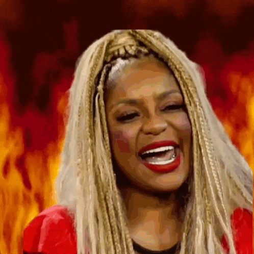 a woman with braids and red lipstick is laughing in front of a fire background .
