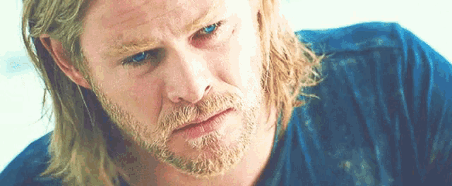 a man with long blonde hair and a beard is wearing a blue shirt and looking down