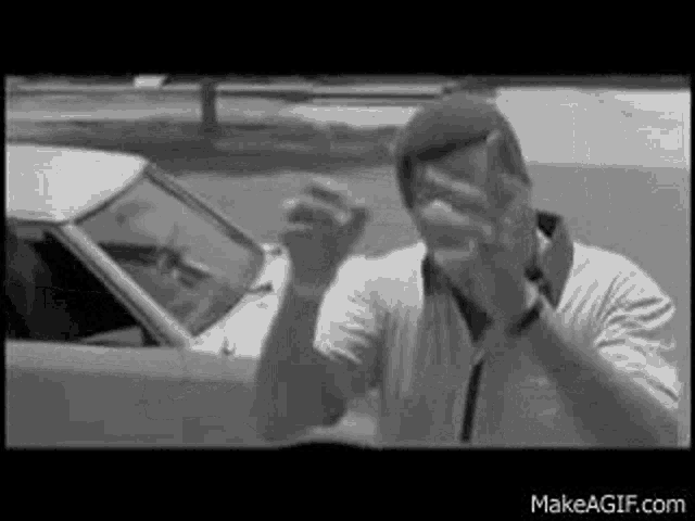 a man is standing in front of a car with his hands up .